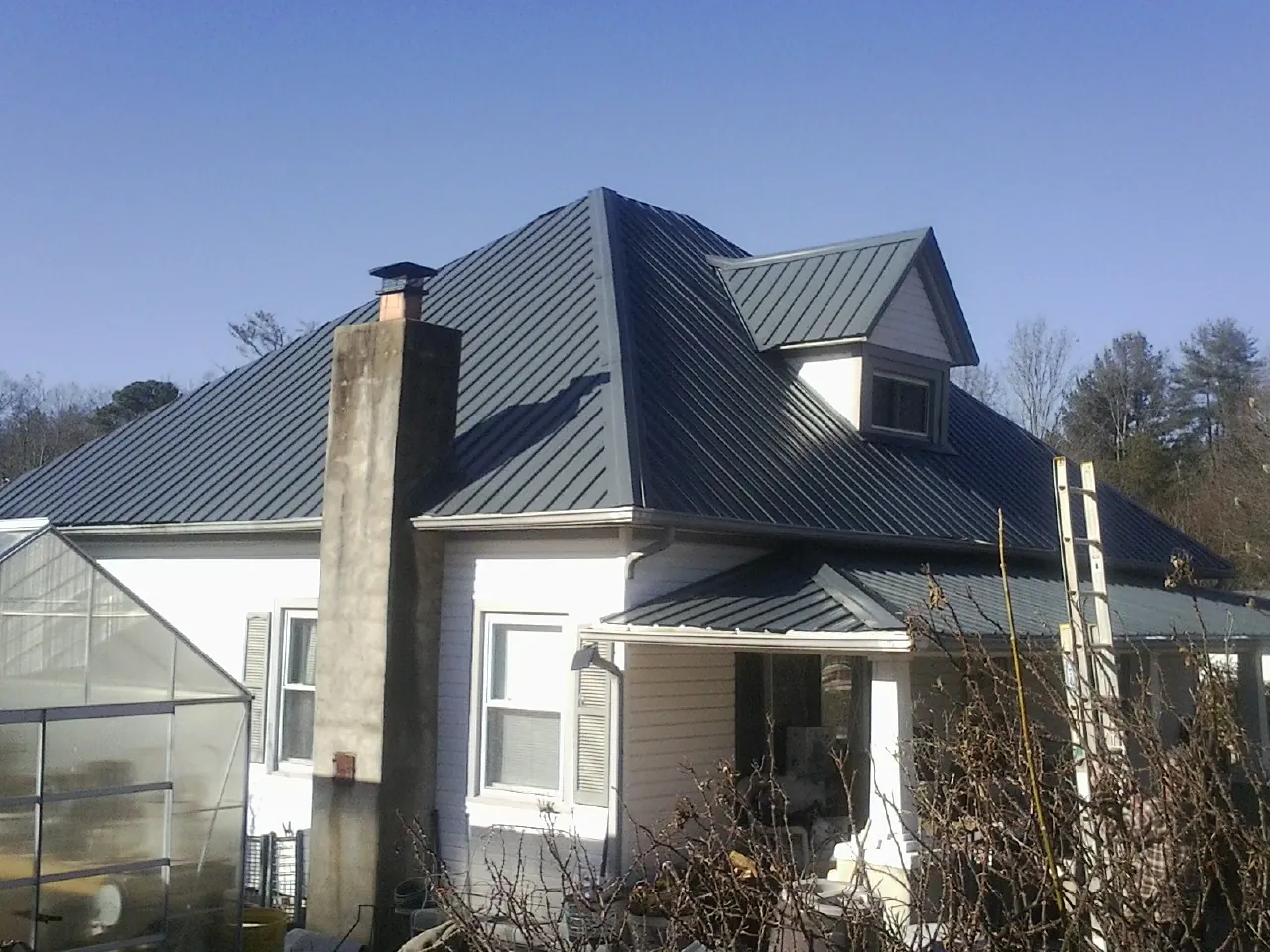 Dark blue standing seam metal roof on a white farmhouse with dormer — Slate & Tile Roof Repair by Roofing Brothers in Fairborn