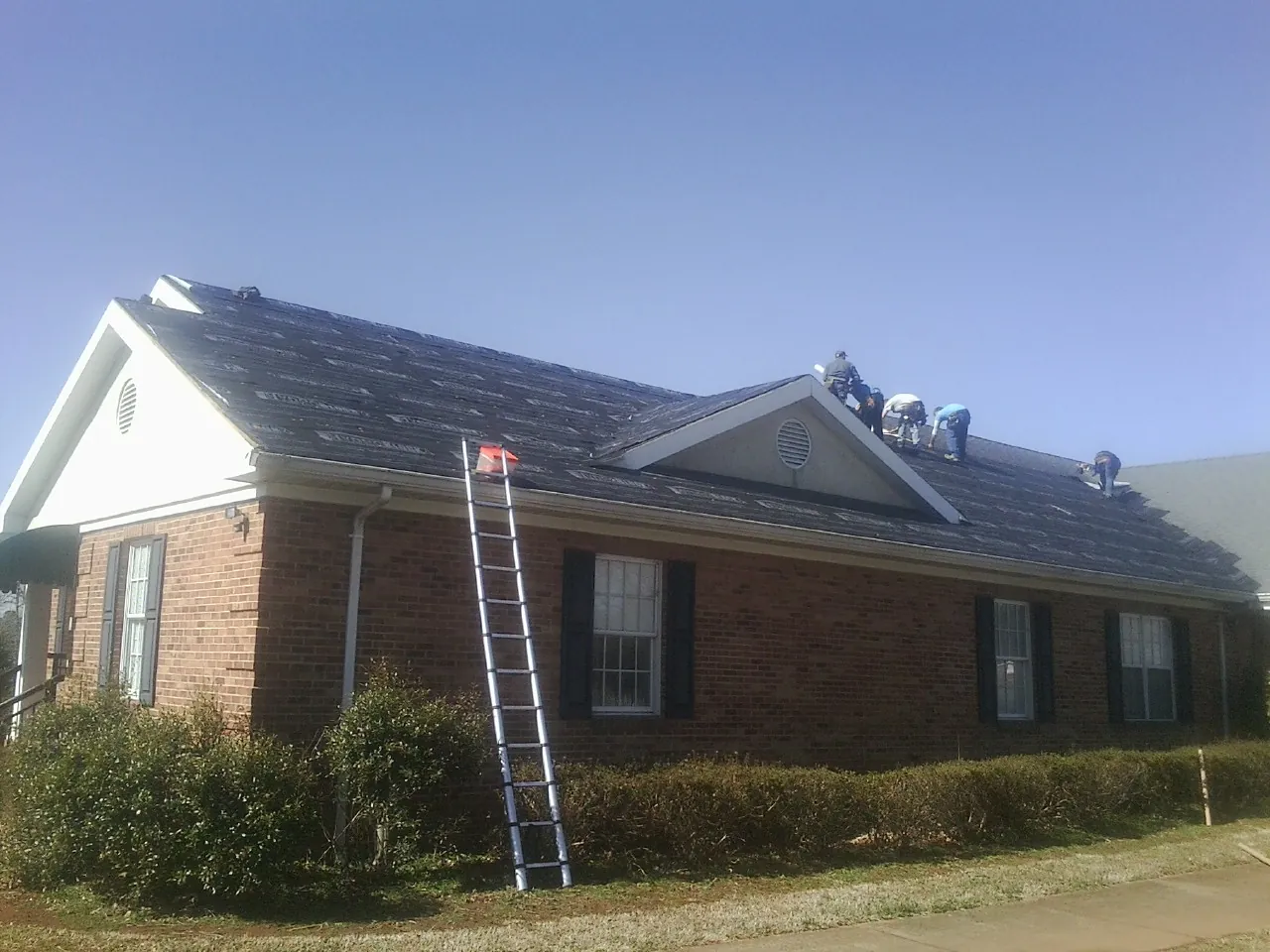 Crew tearing shingles off a brick ranch roof with a ladder set — Metal Roof Repair work by our crew in Fairborn