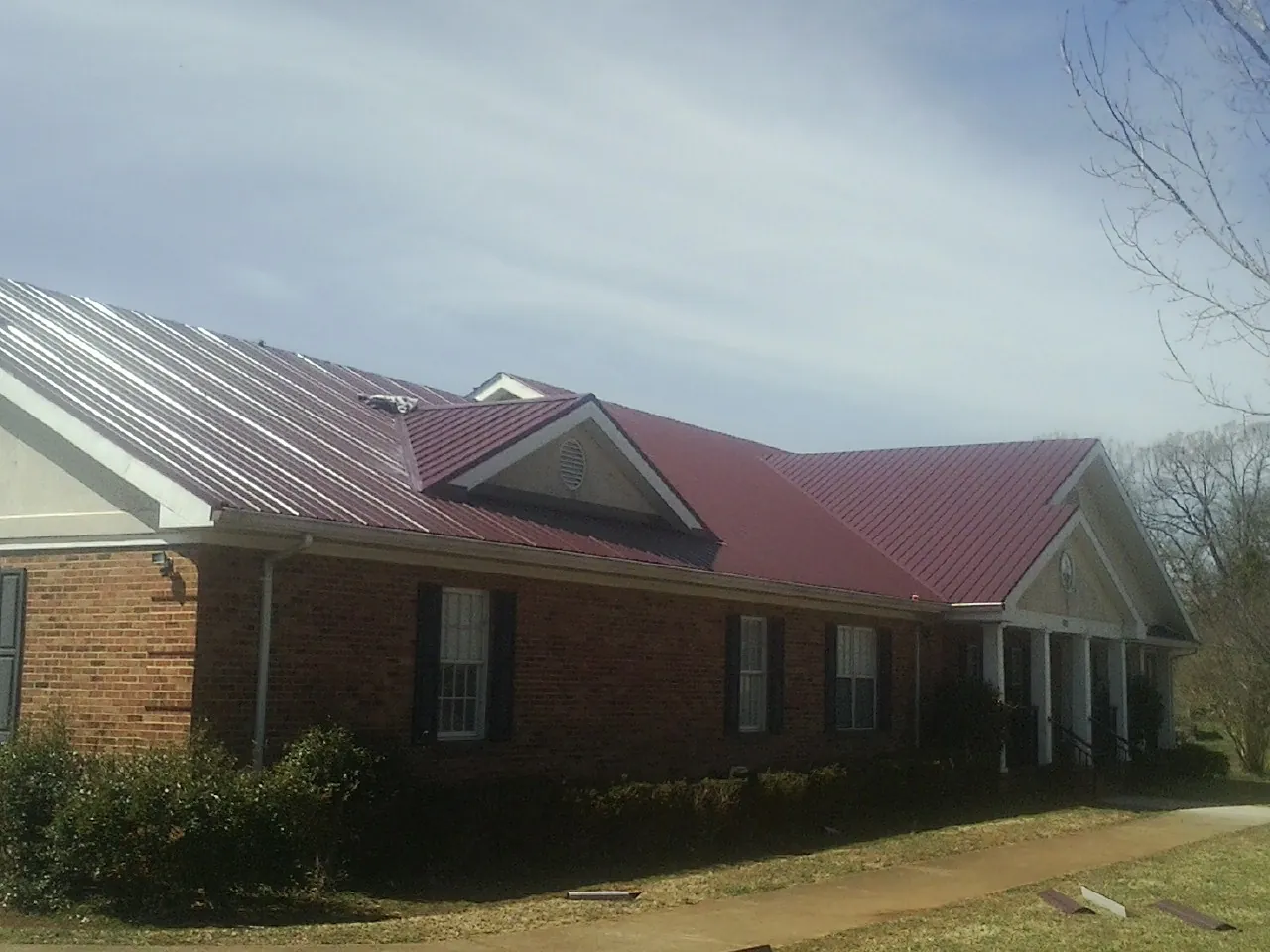 Red metal roof with gabled entries on a long brick building, from a Hail Damage Roof Repair job in Fairborn