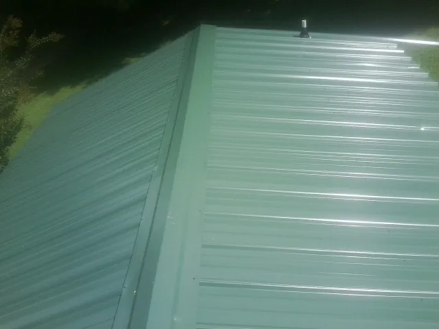 New green metal panels meeting at the ridge of a roof — Flat Roof Repair work by our crew in Fairborn