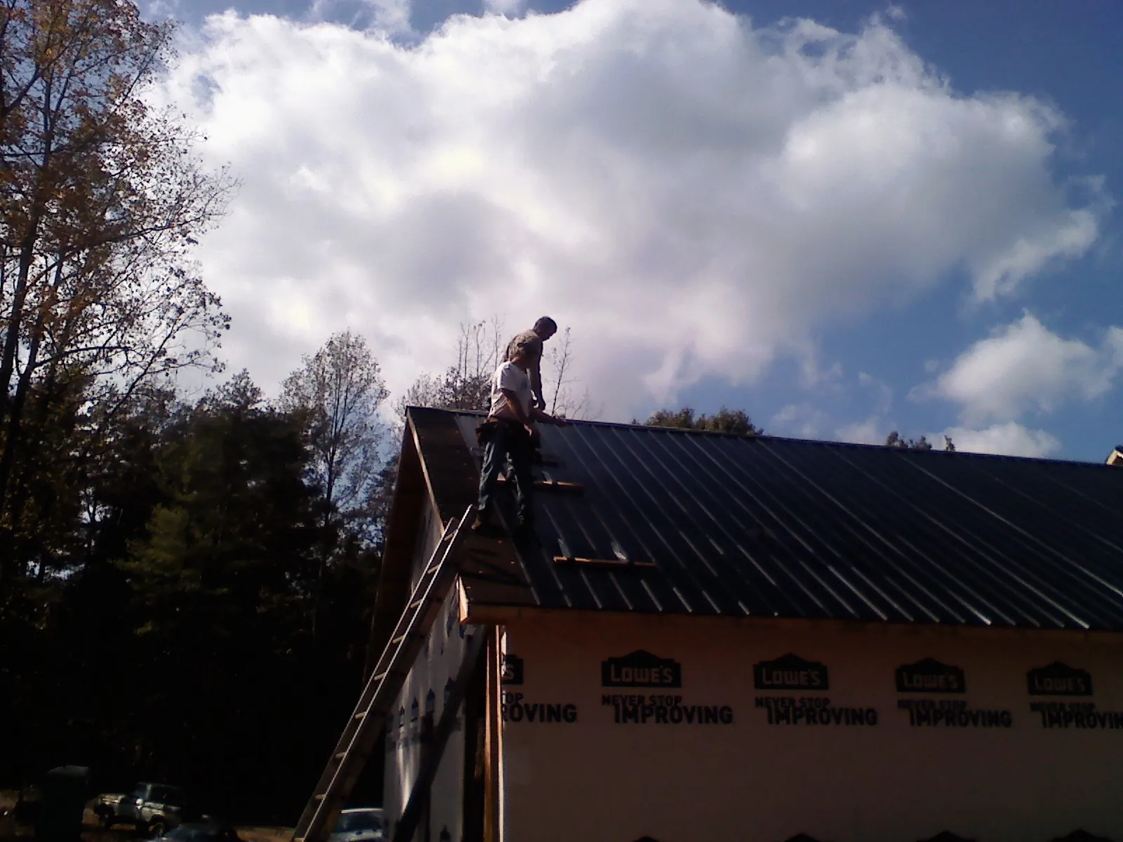 Roofer fastening dark metal panels high against a cloudy sky, from a Roof Inspection job in Fairborn